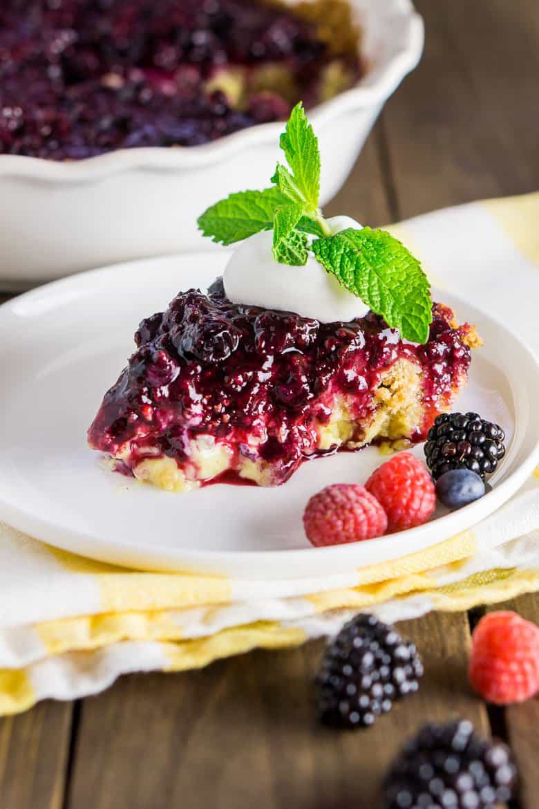 A sliced of berry custard pie on a white plate with fresh fruit on the side.