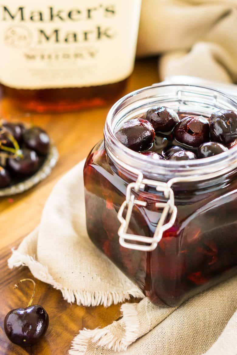 A glass jar of cherry bourbon with a bottle of bourbon in the background.