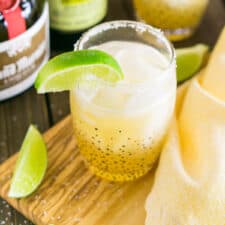 A classic margarita on a wooden tray with bottles of liquor behind it.