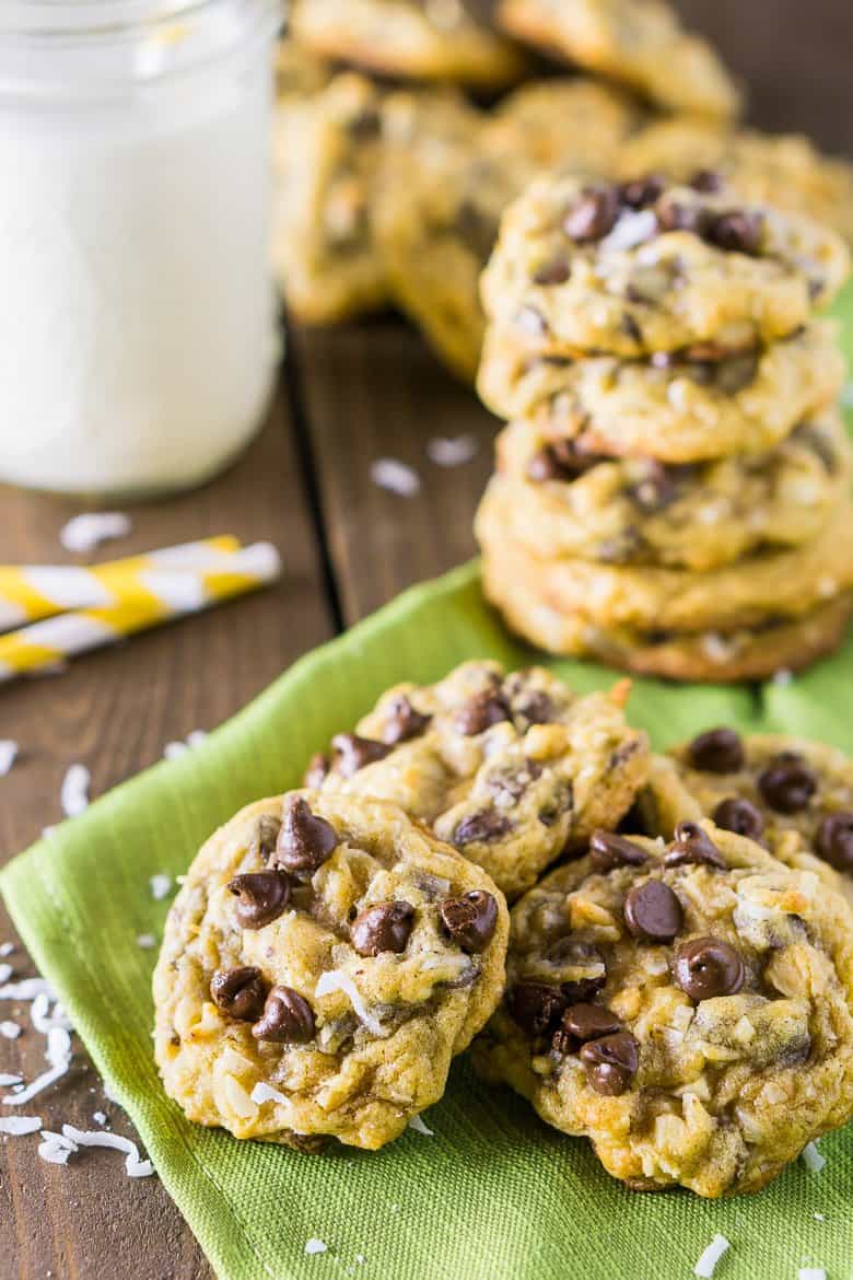 A pile of chocolate chip cookies with coconut around it and a glass of milk.