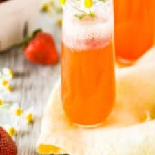 Two roasted strawberry Aperol spritzes with flowers on a yellow napkin.