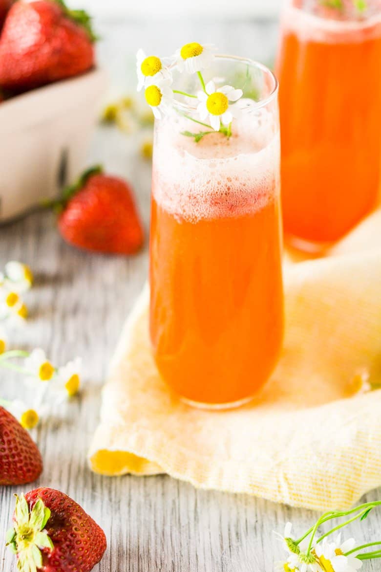 Two roasted strawberry Aperol spritzes with flowers on a yellow napkin.