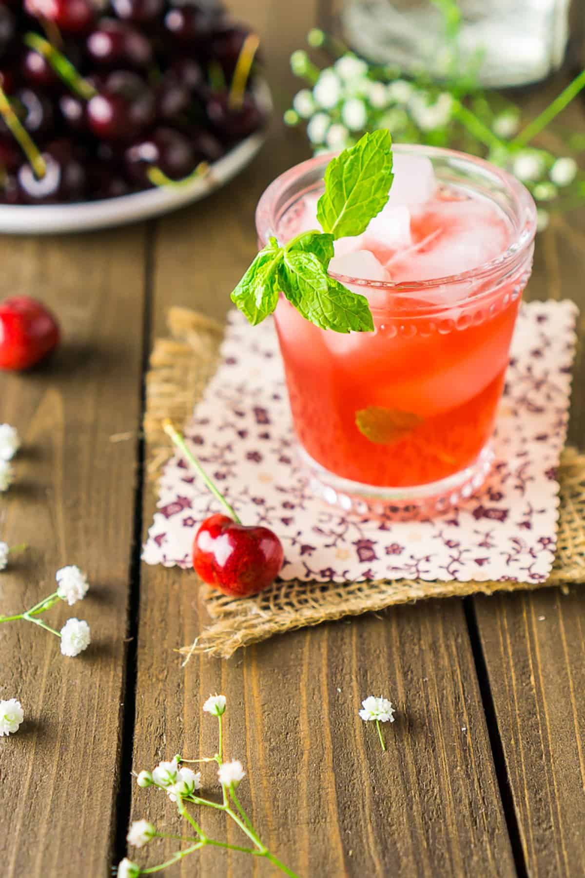 Looking down on a cherry bourbon smash with a plate of fresh cherries to the side on a wooden surface.