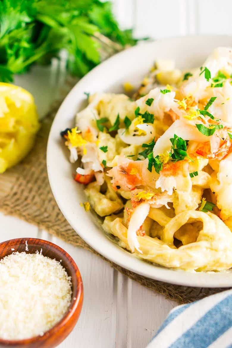 A bowl of grilled lobster Alfredo with Parmesan, lemons and parsley on the side.