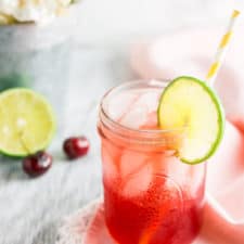 The bourbon cherry limeade on a pink napkin with white flowers behind it.