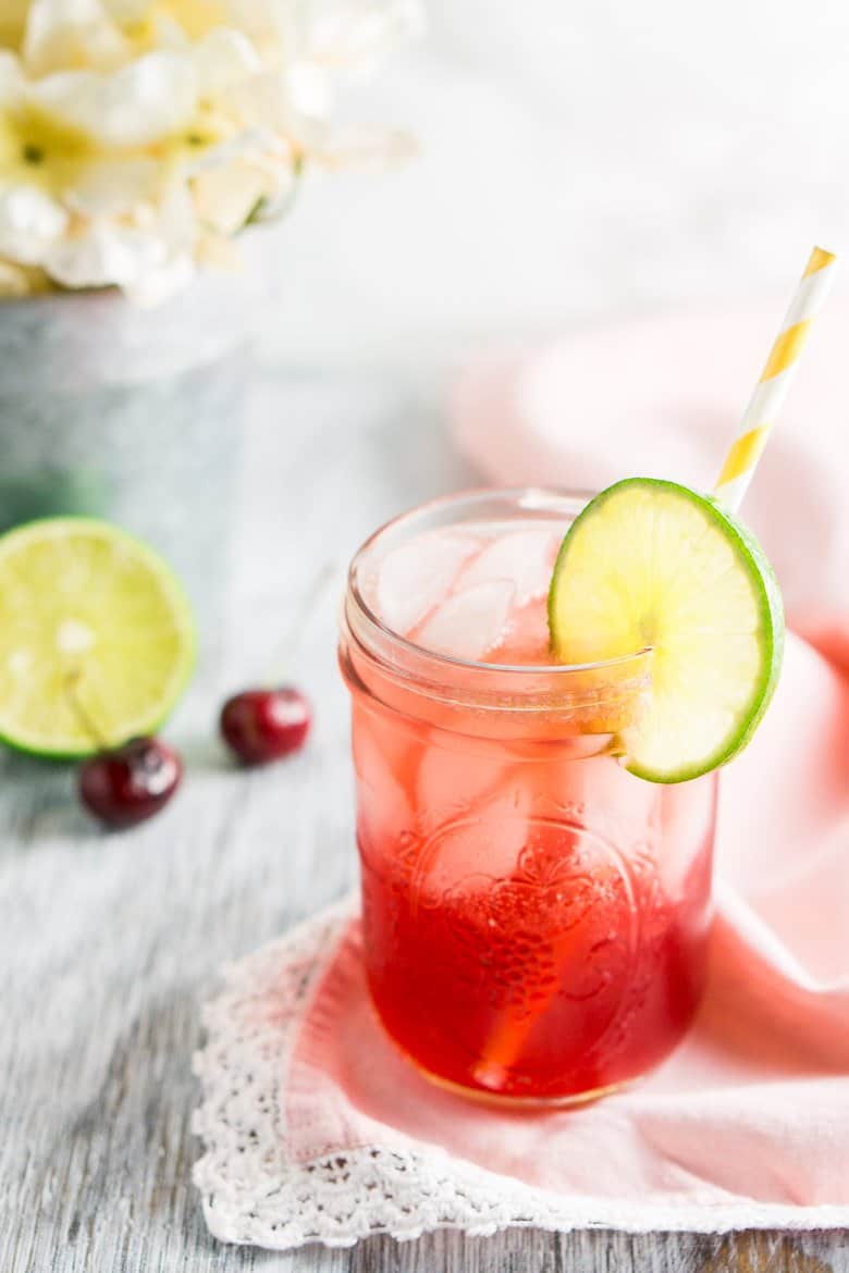 The bourbon cherry limeade on a pink napkin with white flowers behind it.