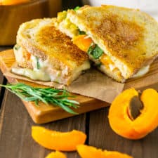 Two halves of Brie grilled cheese with slices of apricots around it.