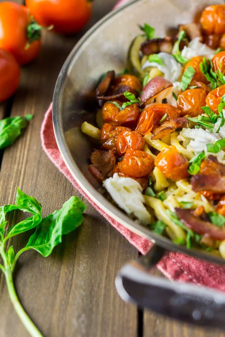 A skillet of caprese carbonara with tomatoes and fresh basil on the side.