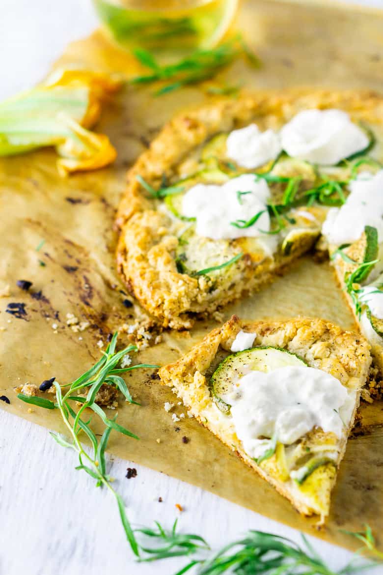 A slice of the burrata zucchini galette on parchment paper with the rest of the galette in the background.