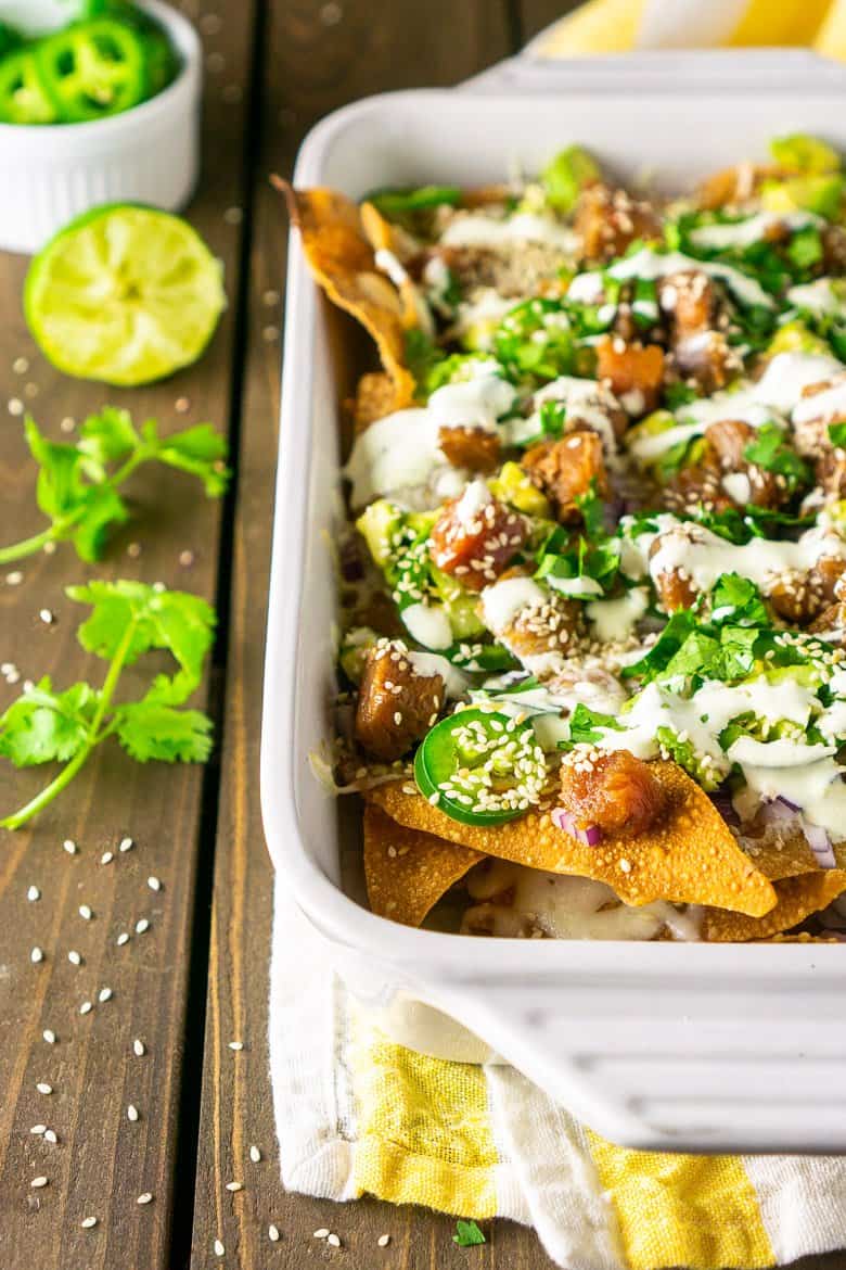 A white baking dish filled with ahi nachos with wasabi Crema with cilantro and lime on the side.