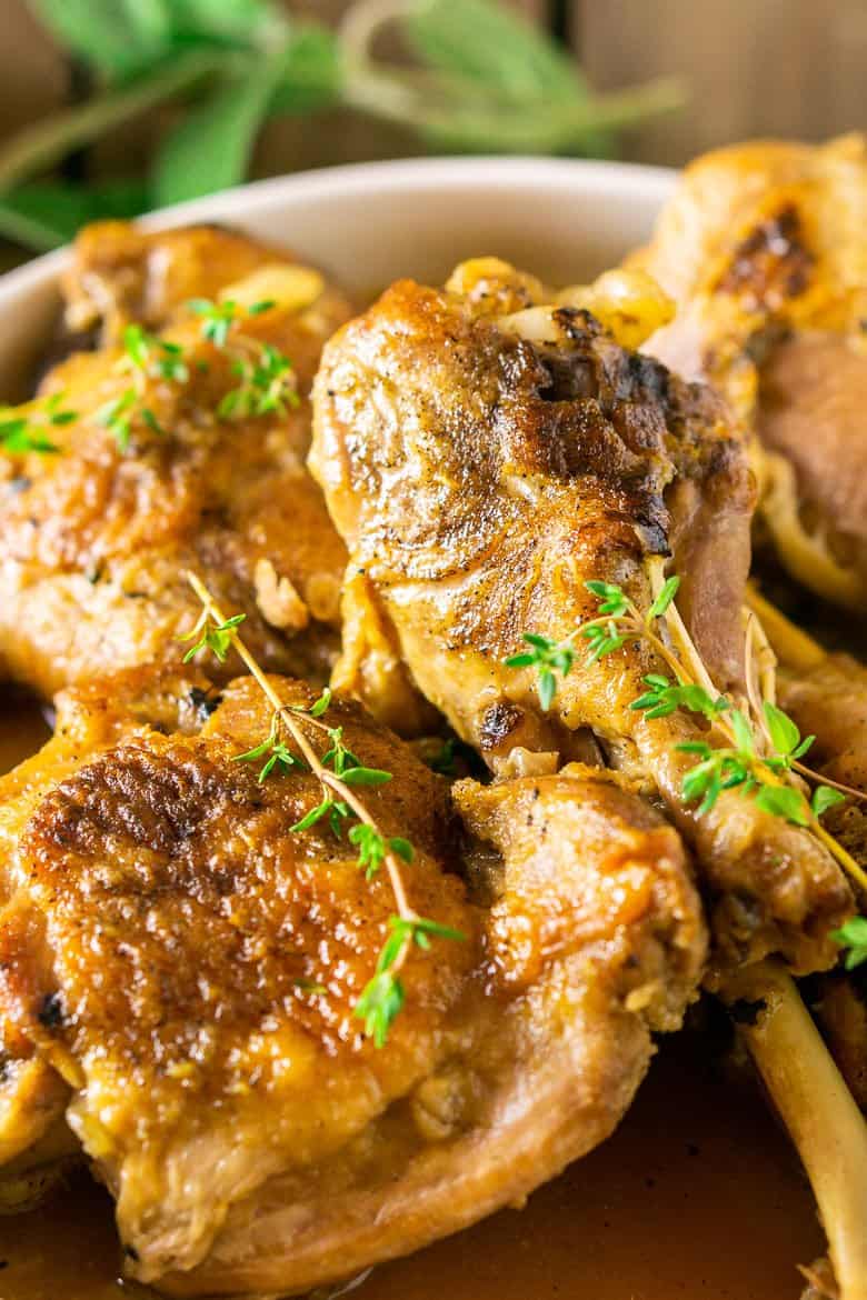 Maple-braised turkey legs and thighs with a focus on the legs on a white platter surrounded by fresh thyme.