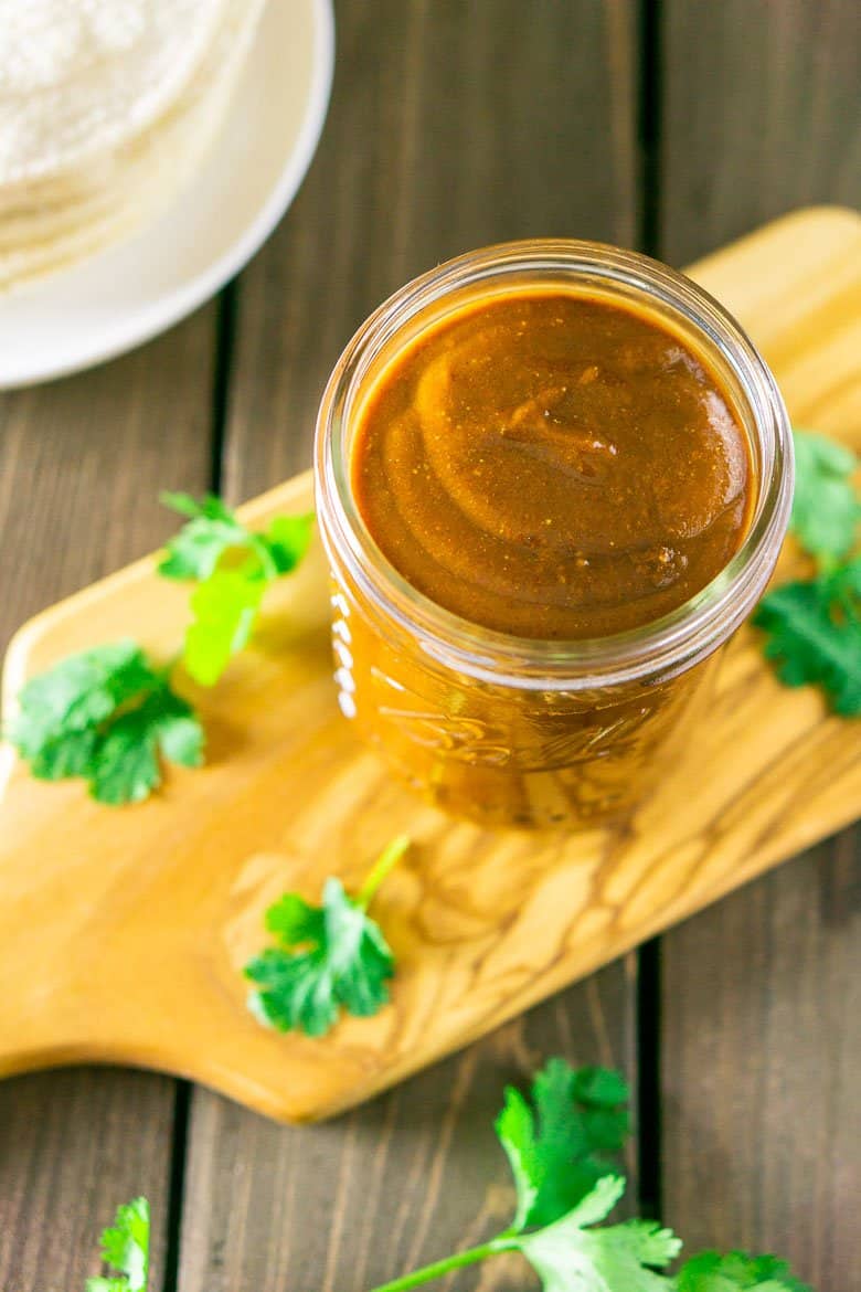 Red enchilada sauce in a mason jar surrounded by cilantro and corn tortillas.