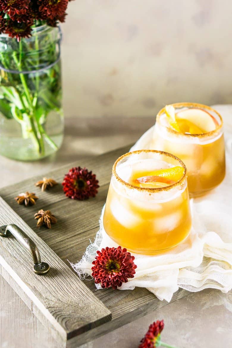 Gingered bourbon-apple cider cocktail with fall flowers and wooden tray