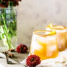 Gingered bourbon-apple cider cocktail with fall flowers and a wooden tray