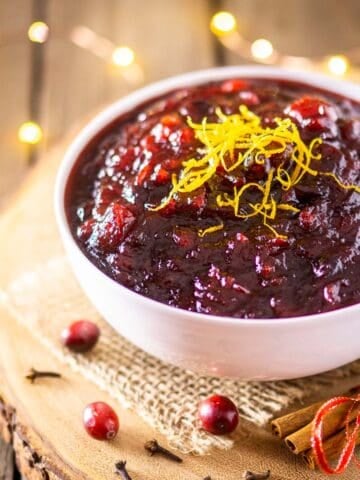 A bowl of brandy cranberry sauce on a wooden platter with twinkle lights behind it.