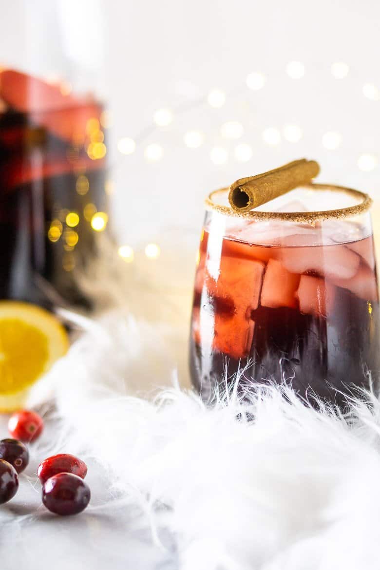 A front view of holiday sangria with cinnamon stick on top and the pitcher in the background.