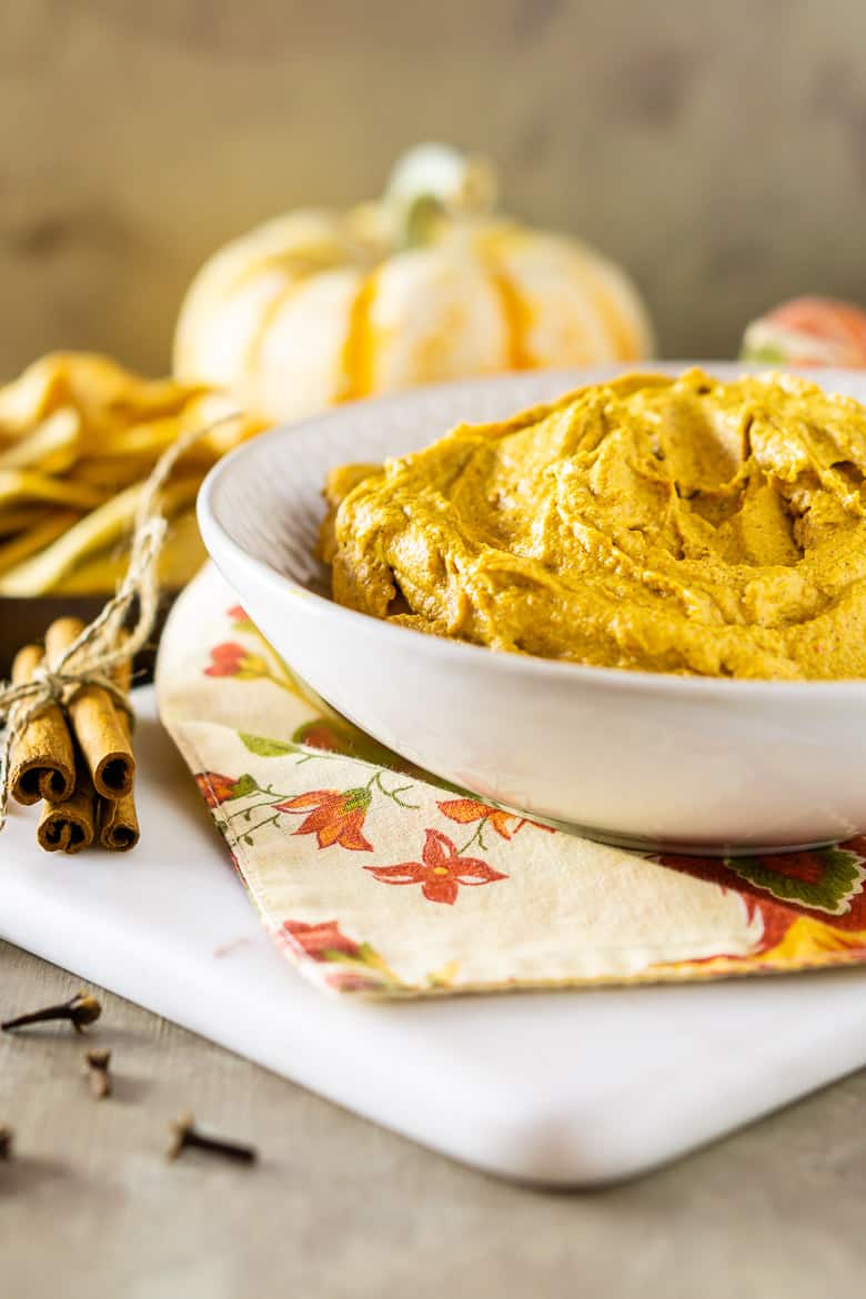 Pumpkin-chipotle hummus on a marble serving tray with pita chips and a pumpkin.