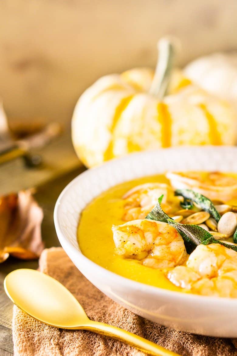 A close-up of pumpkin polenta with brown butter shrimp, pumpkin seeds and fried sage with pumpkins and fall leaves as decor.