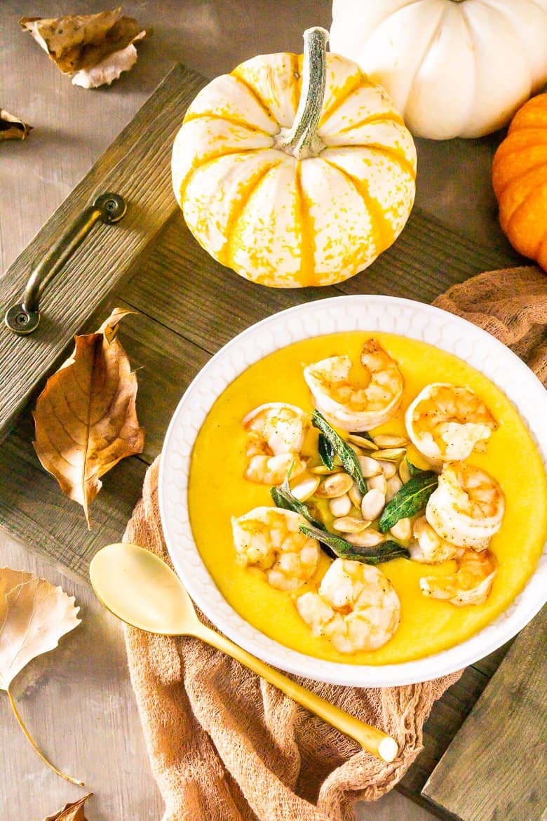 An aerial shot of pumpkin polenta with brown butter shrimp, pumpkin seeds and fried sage with pumpkins and fall leaves as decor.