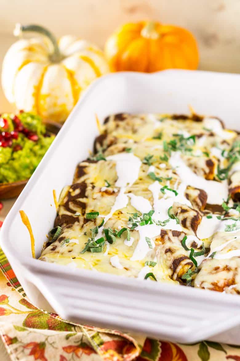 A pan of Thanksgiving enchiladas with pomegranate guacamole and pumpkins as decor.