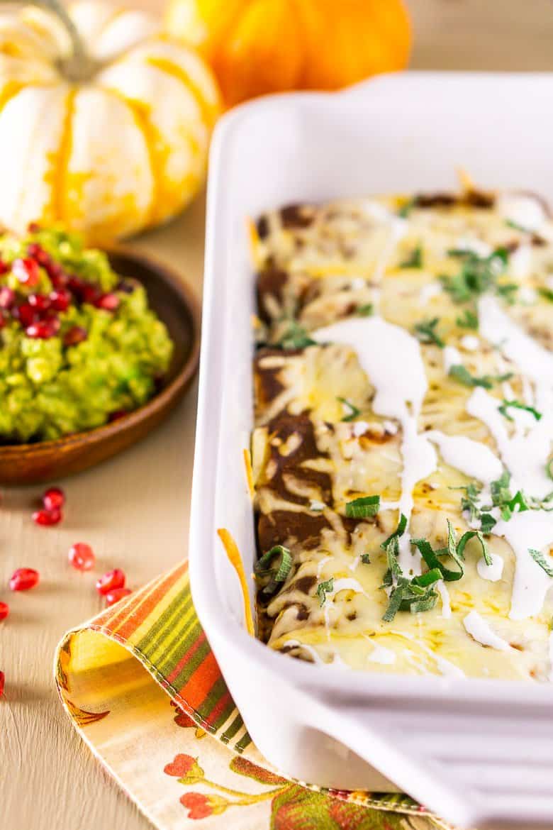 A pan of Thanksgiving enchiladas with pomegranate guacamole and pumpkins as decor