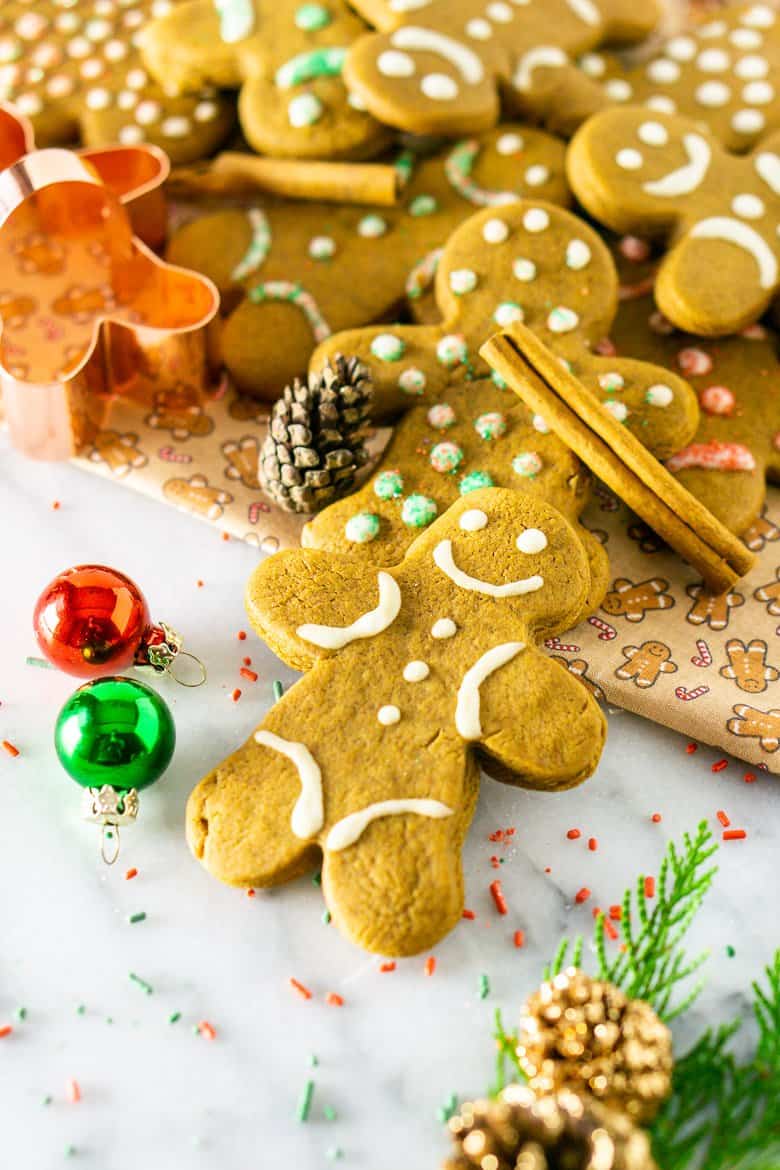 A pile gingerbread men cookies with Christmas decor and a cookie cutter.