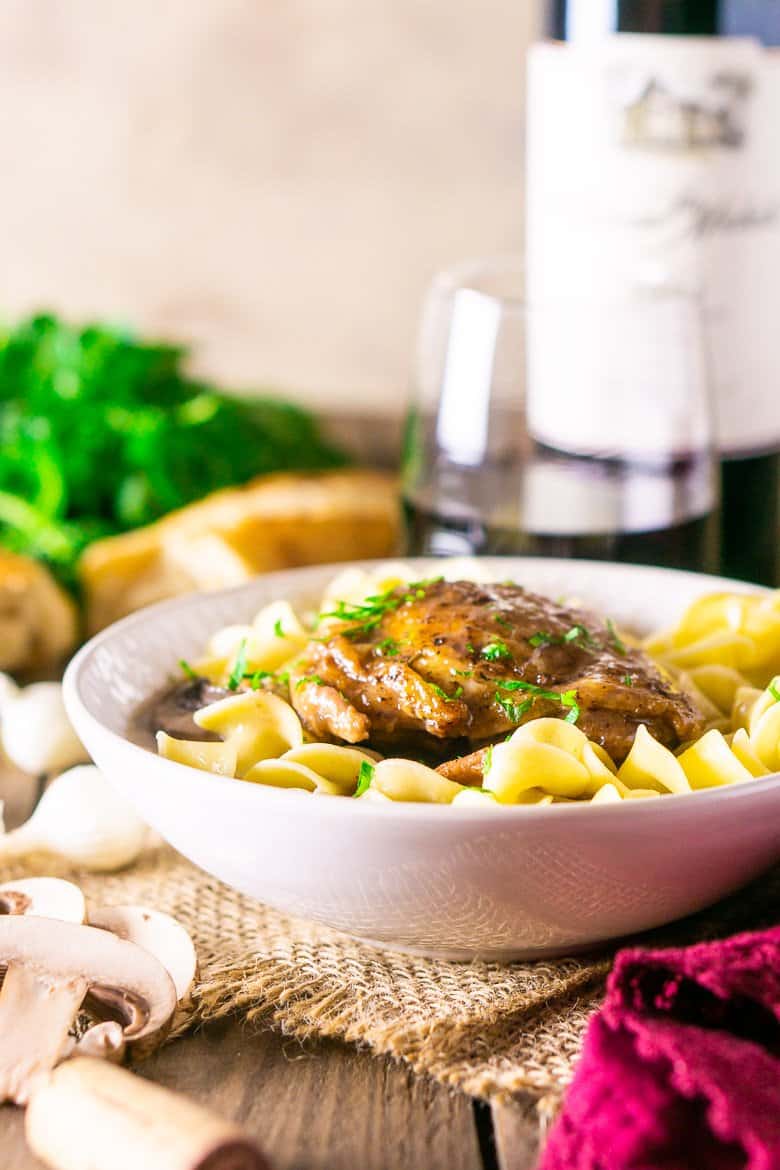 A front view of the coq au vin with a bottle of wine.