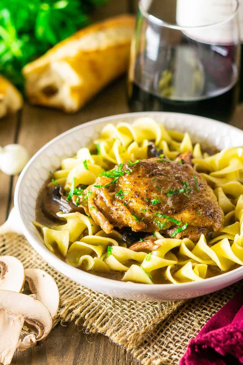 A close-up of the coq au vin with mushrooms, bread and a glass of wine.