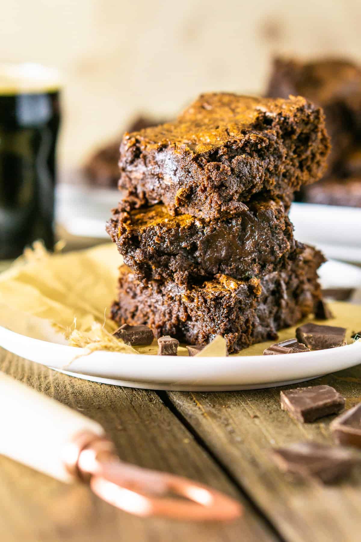 A stack of fudgy stout brownies on a white plate with parchment paper.