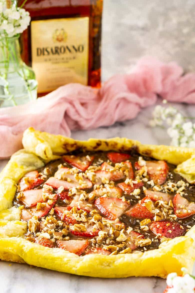 The amaretto strawberry Nutella puff pastry tart with flowers and a bottle of amaretto.