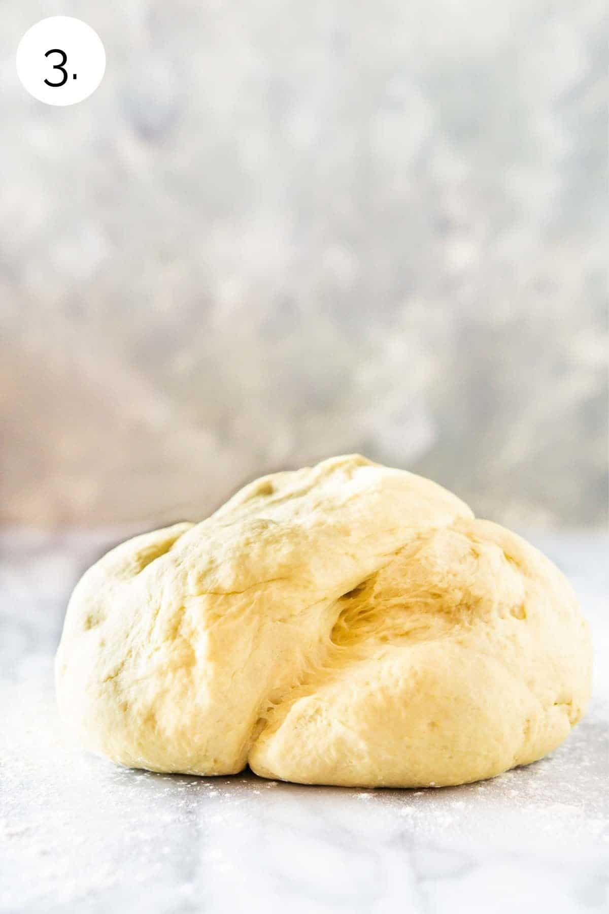 A ball of smooth, elastic, tacky dough after it's been kneaded on a pastry board.