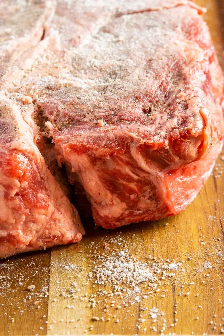 The chuck roast dusted with flour, salt and pepper sitting on a wooden cutting board.