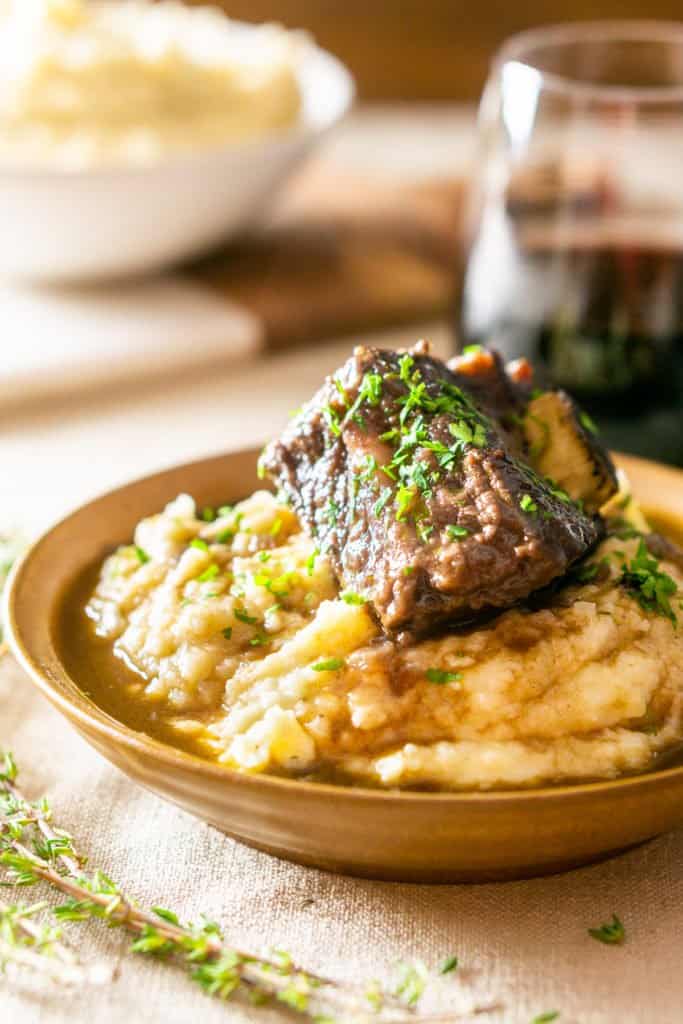A bowl of brown butter mashed potatoes with a braised red wine short rib on top with a glass of wine.