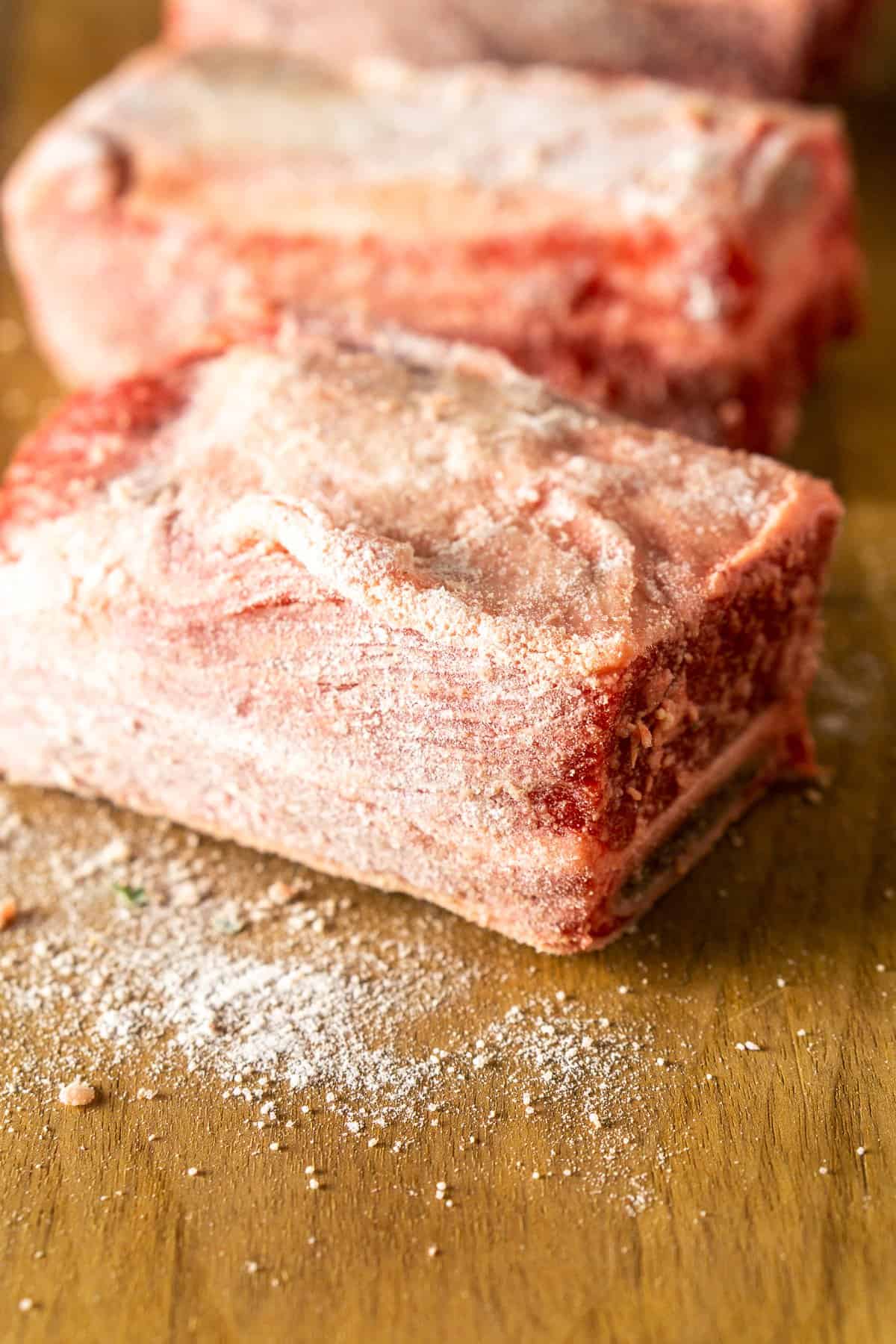 The short ribs on a wooden cutting board after being dusted with flour, salt and pepper.