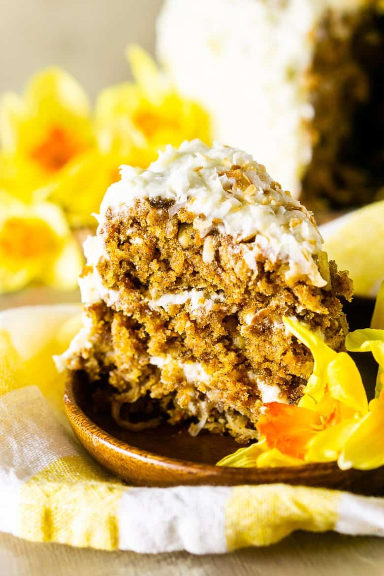 A side view of the homemade carrot cake with the full cake in the background.