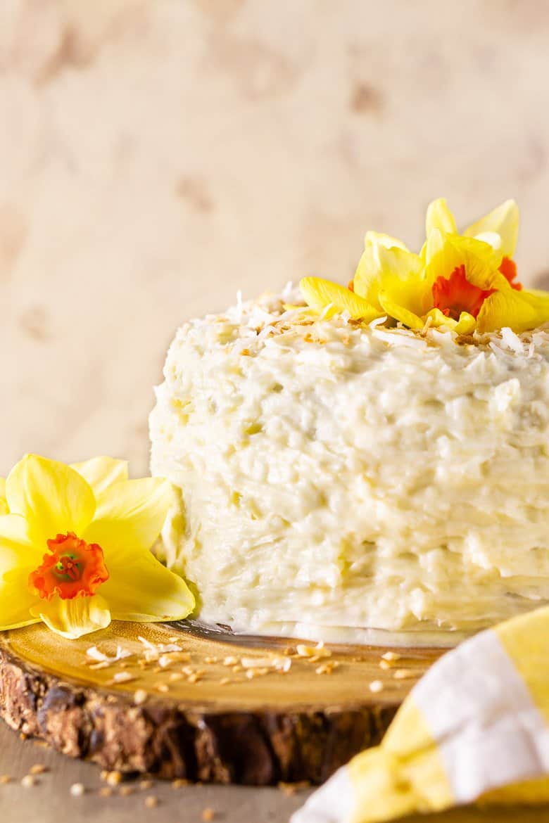 The homemade carrot cake frosted in coconut cream cheese frosting on a wooden cake stand.