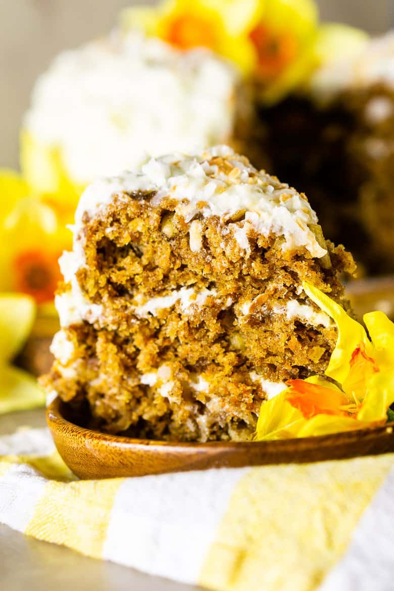 A slice of homemade carrot cake with the full cake in the background.