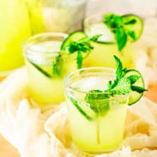 Three glasses of mint-cucumber lemonade with flowers and a carafe.