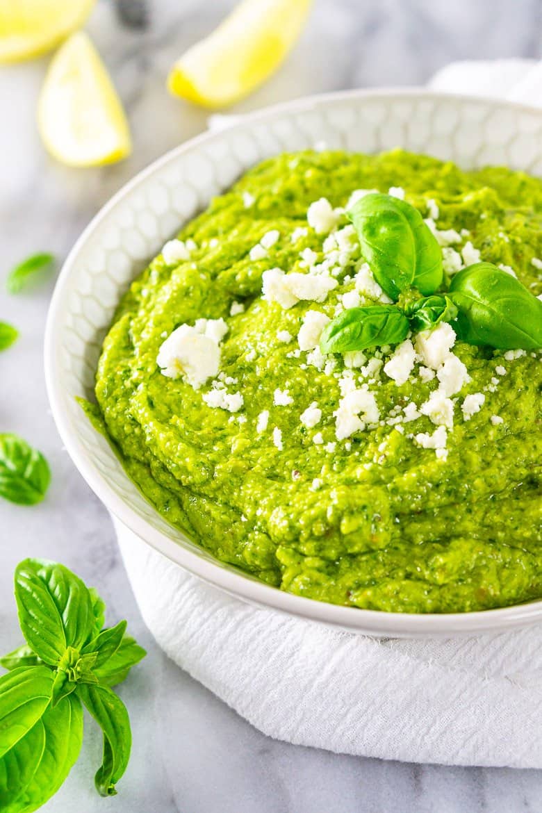 A bowl of feta-avocado pesto sauce with cut-up lemons.