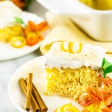 A slice of spiced orange tres leches cake with the full cake and flowers in the background.