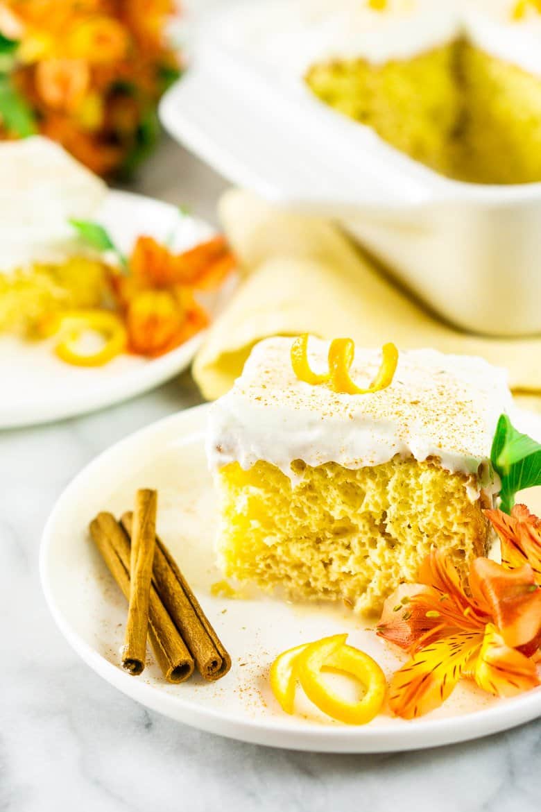 A slice of spiced orange tres leches cake with the full cake and flowers in the background.