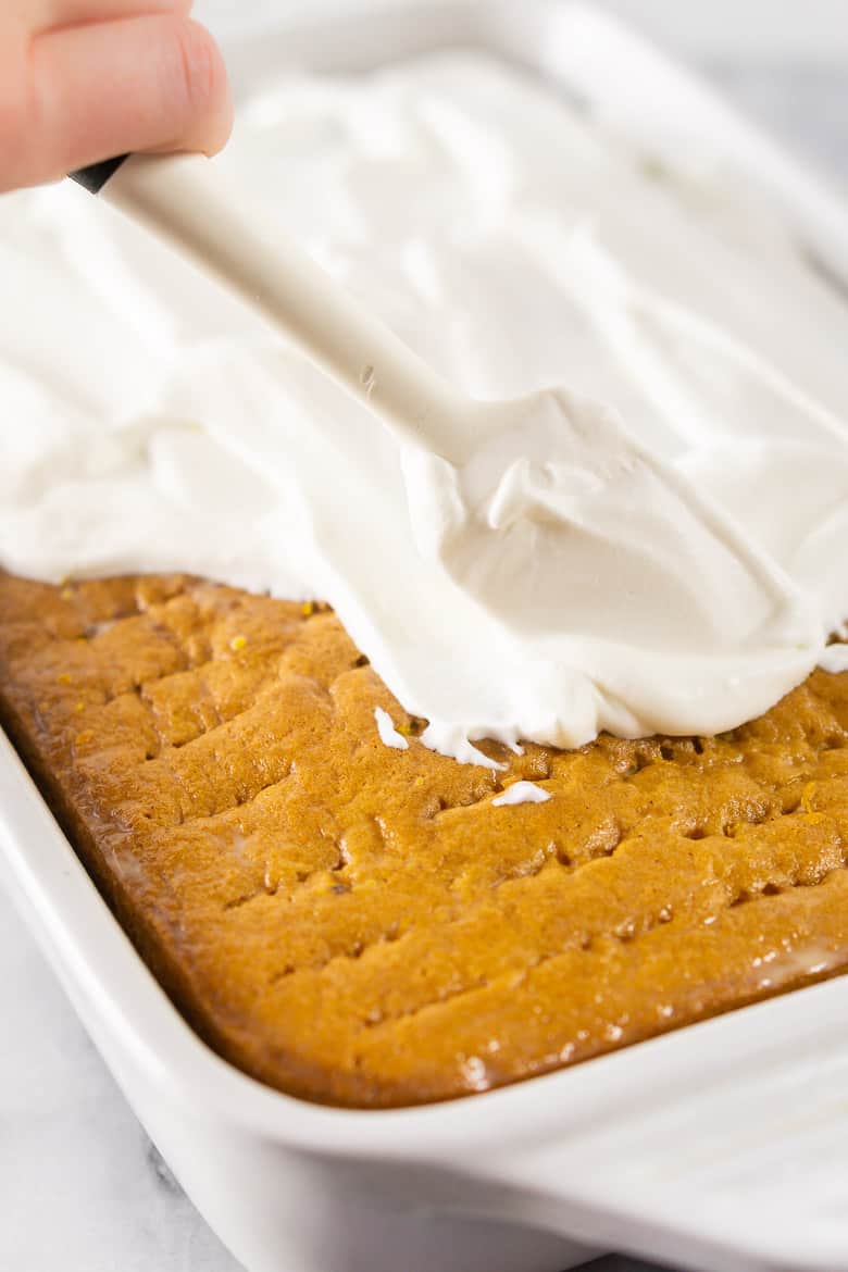 A hand spreading the whipped topping onto the spiced orange tres leches cake.