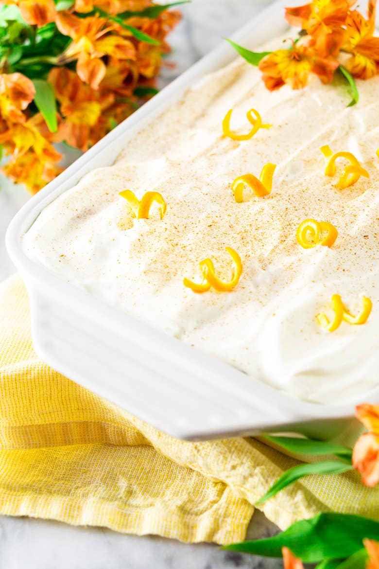 A pan of spiced orange tres leches cake on a yellow napkin with flowers.