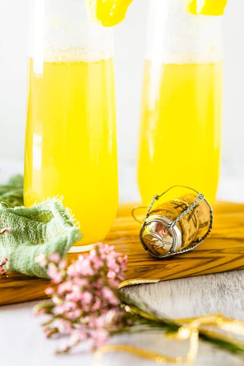 A closeup of a Champagne cork with pineapple mimosas in the background.