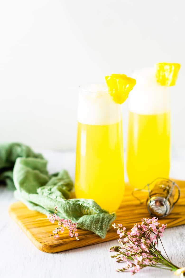 Two pineapple mimosas on a wooden board with flowers.