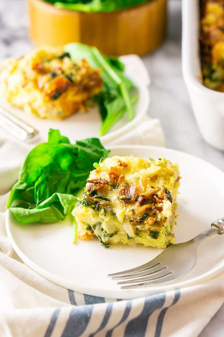 A closeup of a piece of bacon, Gruyere and spinach strata on a white plate.