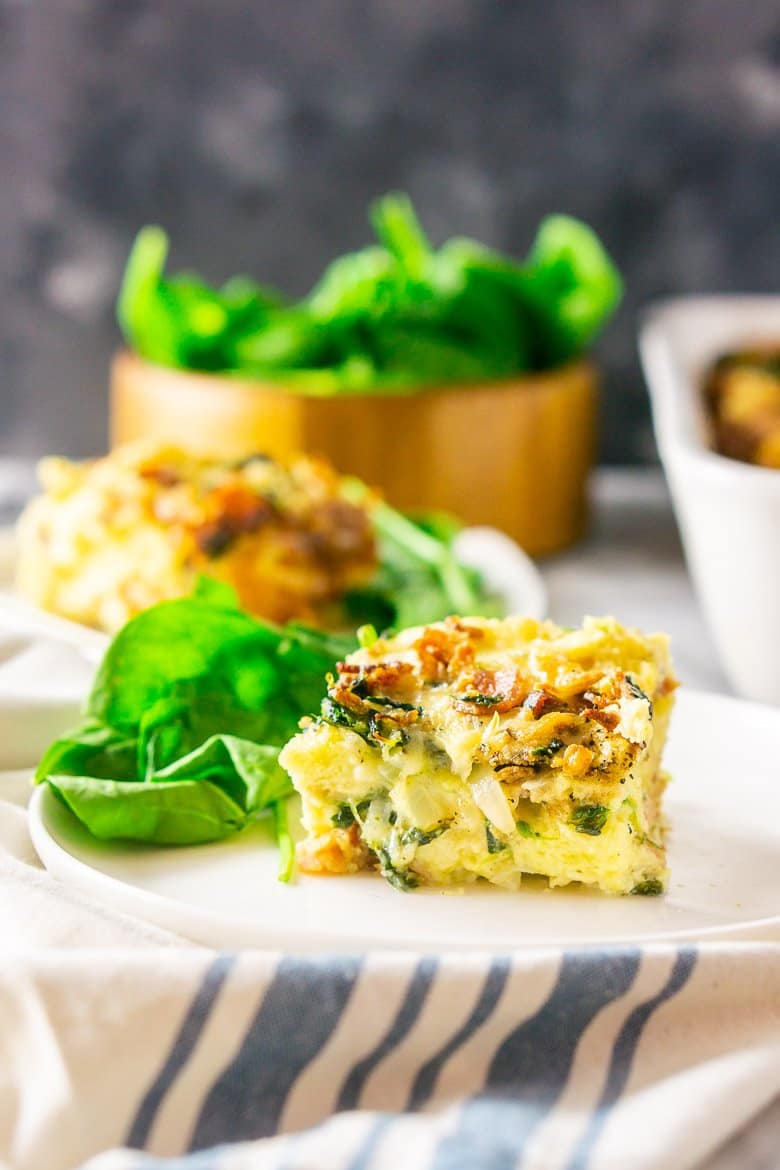 A front view of a piece of bacon, Gruyere and spinach strata with the pan in the background.