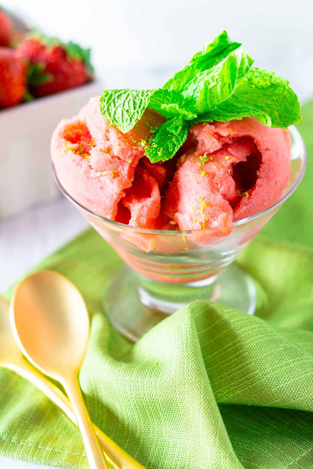 A close-up of the strawberry mojito sorbet on a green napkin with gold spoons to the side.