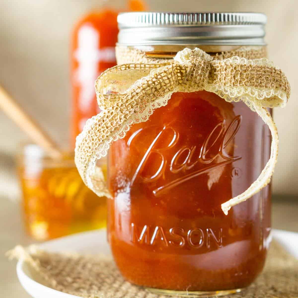 A jar of honey-sriracha BBQ sauce with a burlap ribbon on a plate with a spoonful of sauce.
