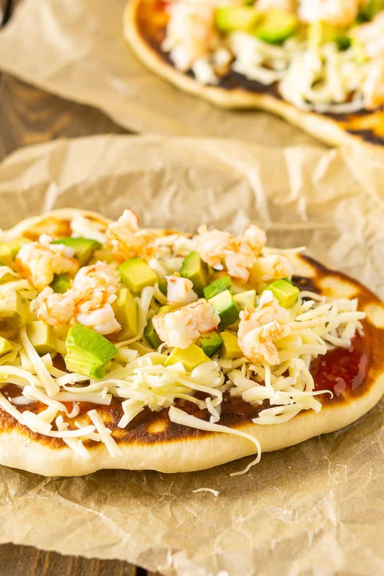 A piece of naan topped with BBQ sauce, cheese, shrimp and avocado.